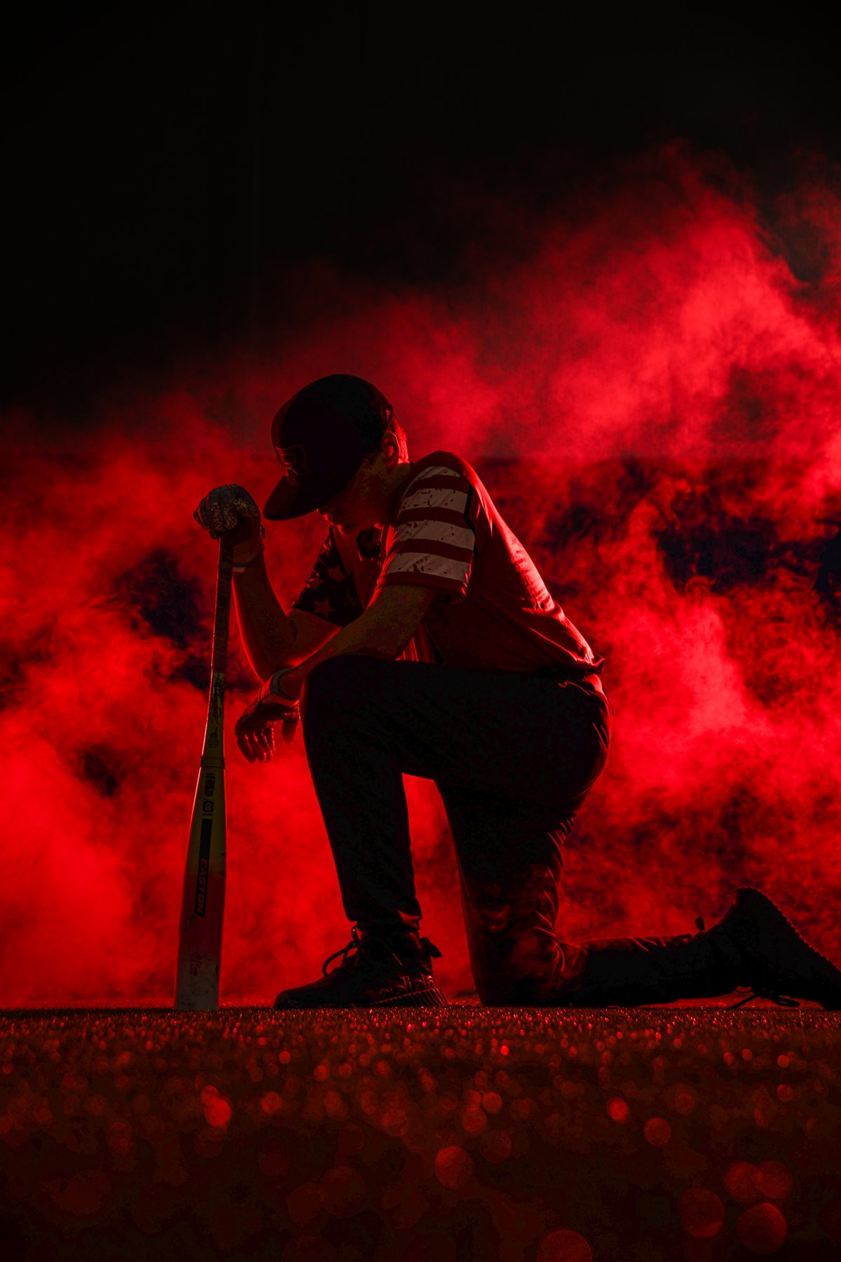 Baseball player kneeling in dramatic red smoke — cinematic sports portrait